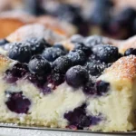 Close-up of a fluffy blueberry cottage cheese breakfast bake slice topped with fresh blueberries and powdered sugar