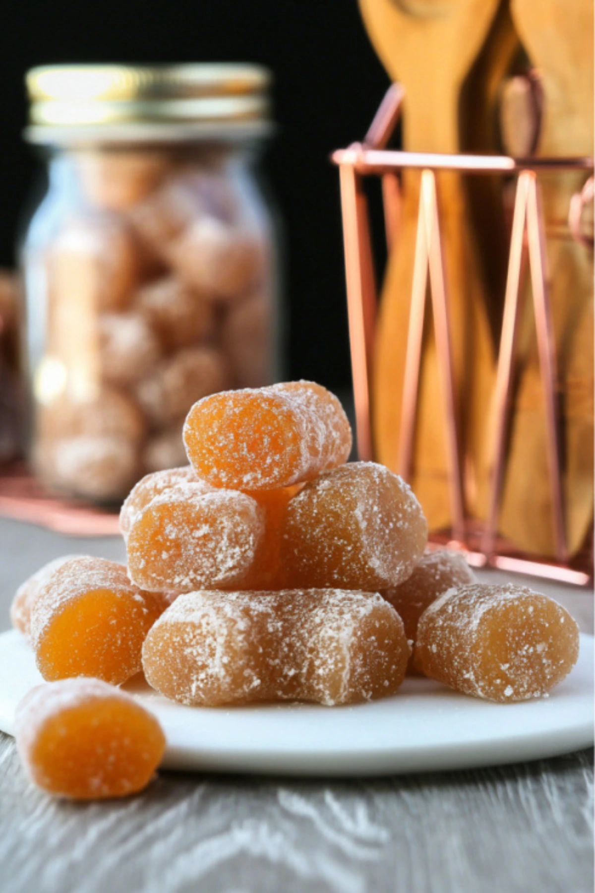 Homemade honey ginger chews candy dusted with cornstarch arranged on white plate with mason jar storage