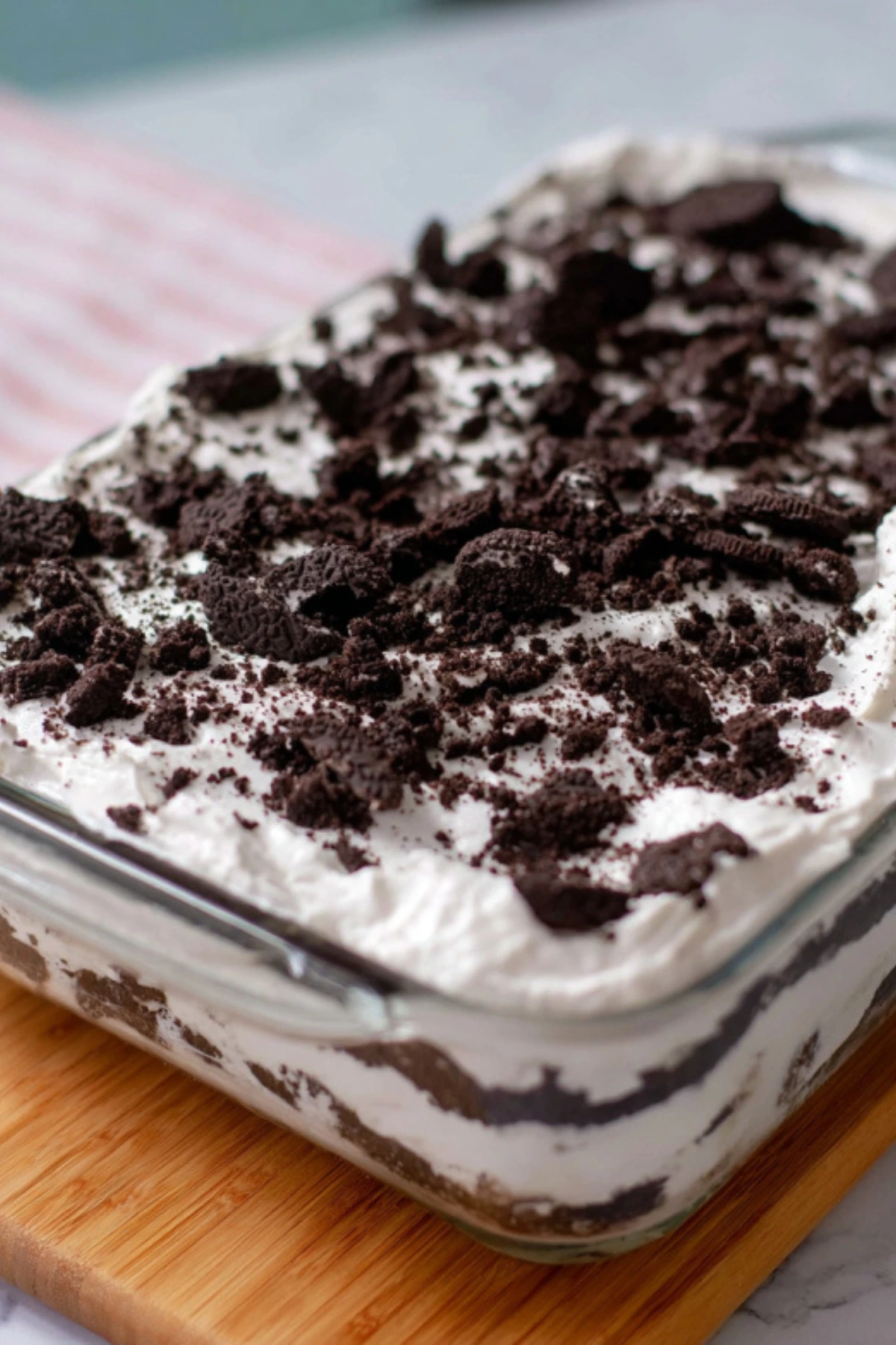 Easy homemade Oreo ice cream cake with layers of crushed cookies, ice cream, fudge sauce and whipped cream in glass baking dish