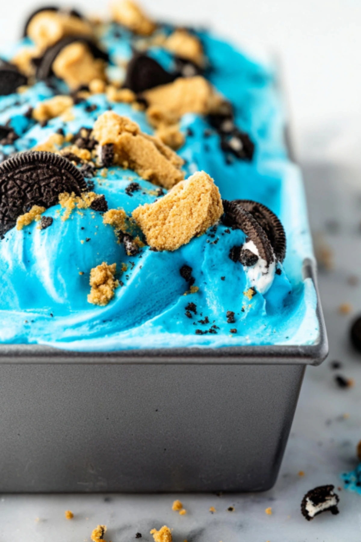 Homemade Cookie Monster blue ice cream in loaf pan topped with chocolate sandwich cookies and graham cracker crumbs