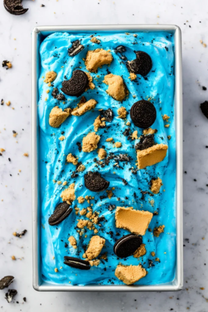 Bright blue Cookie Monster ice cream in metal loaf pan with whole Oreo cookies and graham cracker chunks mixed throughout
