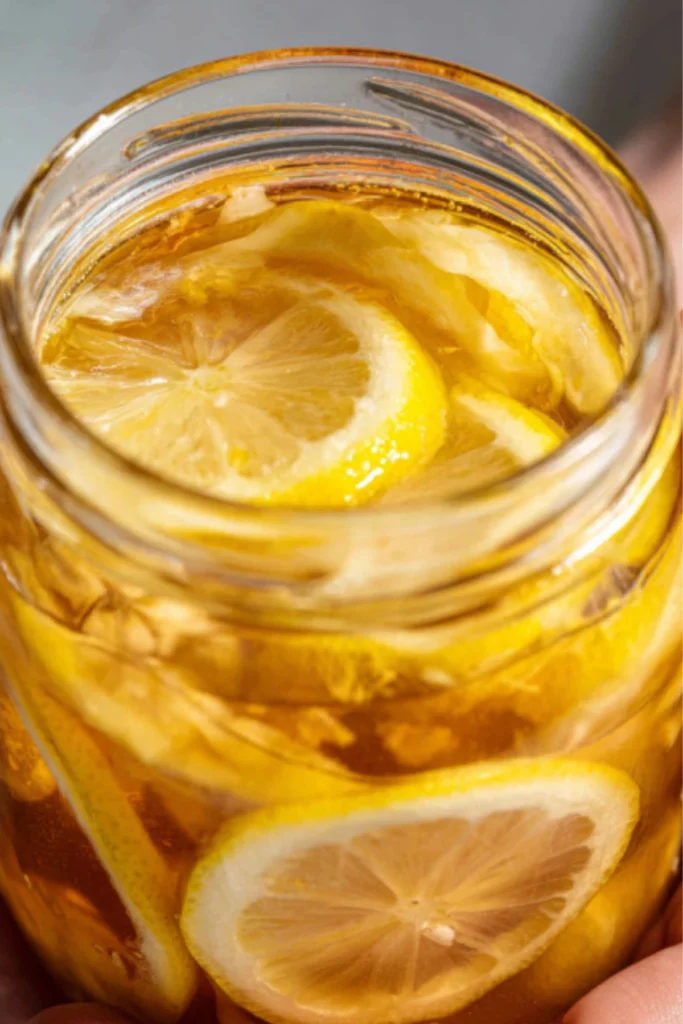 Close-up of golden honey fermented lemon slices in glass jar showing translucent citrus wheels preserved in amber liquid