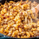 Bacon cheeseburger casserole with melted cheese and ground beef in cast iron skillet with wooden spoon