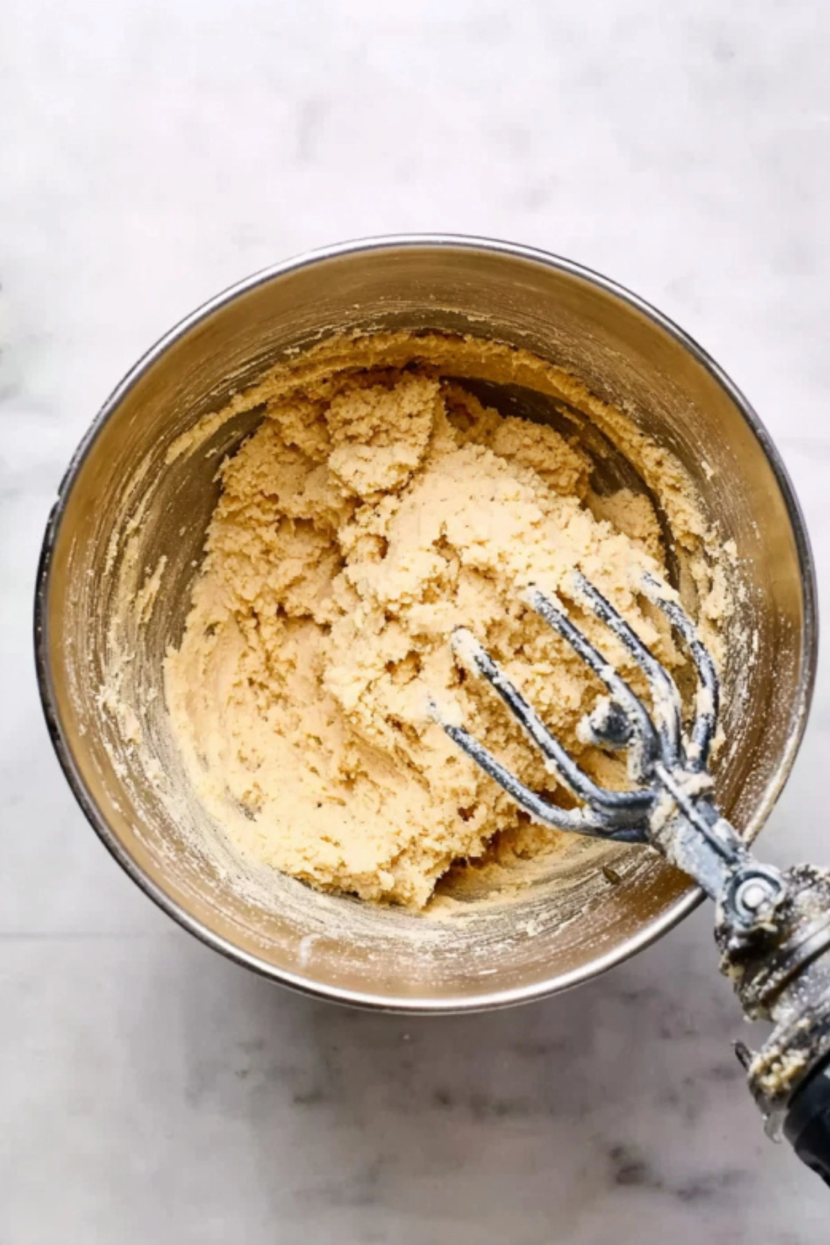 Hand mixer beating white chocolate macadamia nut cookie dough in stainless steel bowl