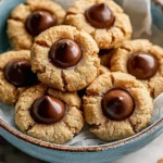Golden peanut butter cookies with chocolate candy centers arranged in a blue ceramic bowl on parchment paper