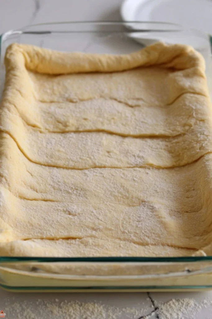 Second tube of crescent dough unrolled and placed over the cheesecake layer in a glass baking dish, with flour sprinkled on top.