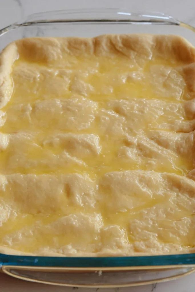 Melted butter evenly poured over crescent dough in a baking dish, preparing it for the perfect golden crust in the churro cheesecake.