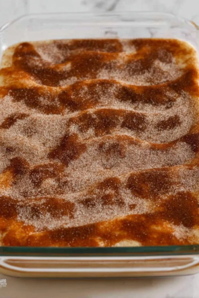 Sprinkling cinnamon sugar on top of churro cheesecake before baking, creating a sweet and crunchy topping.