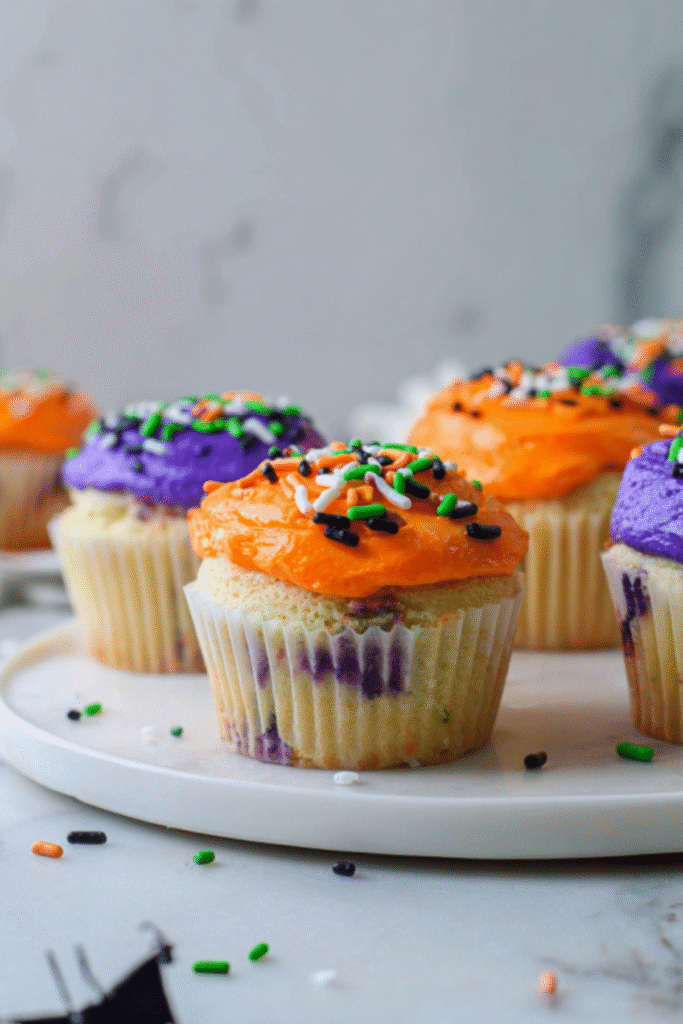 Halloween cupcakes with orange and purple frosting and festive sprinkles on marble background