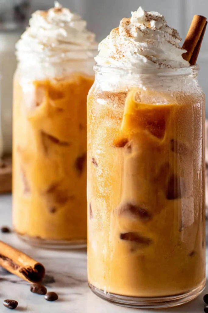 Two jars of iced pumpkin spice latte cold brew with whipped cream, cinnamon, and cinnamon sticks.