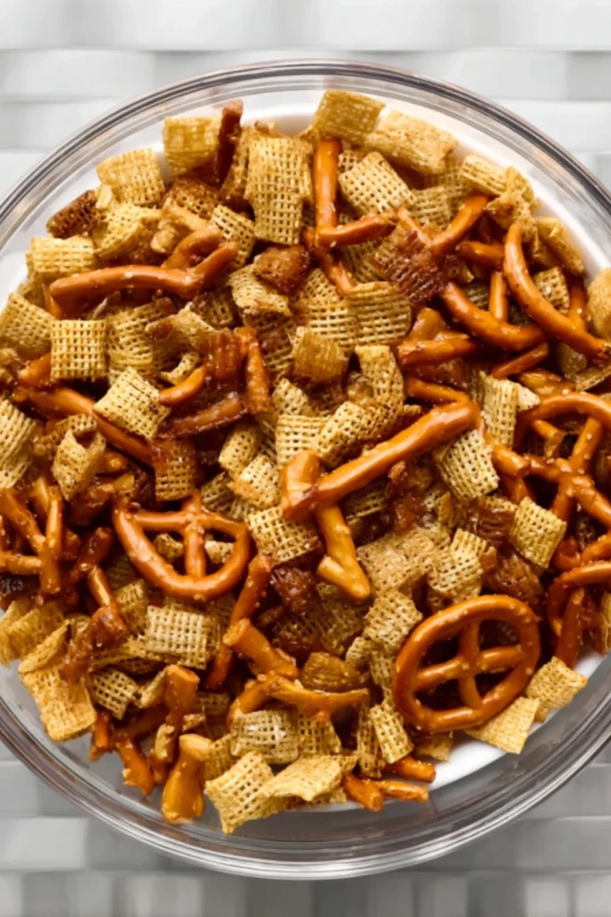 Overhead view of Halloween Harvest Snack Mix base with Chex cereal and pretzels in a glass bowl before adding candy.