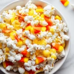 Candy Corn Popcorn Mix in a white bowl with candy corn scattered on marble countertop