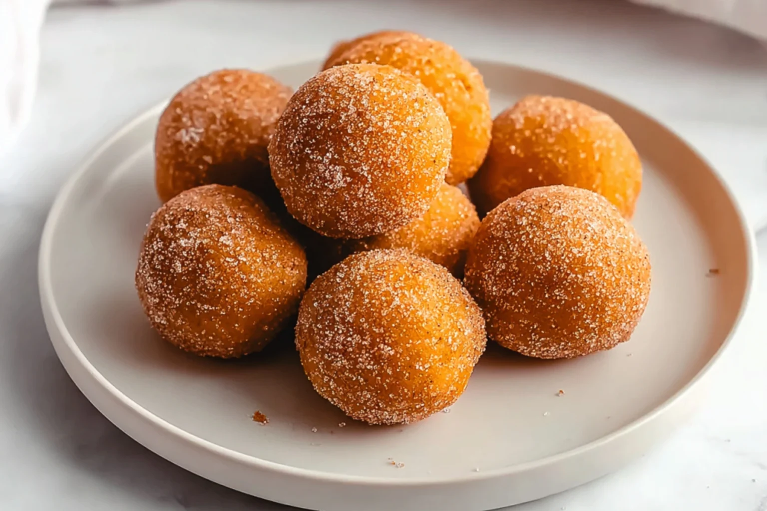 Keto Pumpkin Fat Bombs stacked on a white plate coated with cinnamon spice and sweetener
