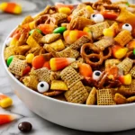 Halloween Harvest Snack Mix with Chex cereal, pretzels, candy corn, pumpkins, Reese’s Pieces, and candy eyeballs in a white bowl on marble.