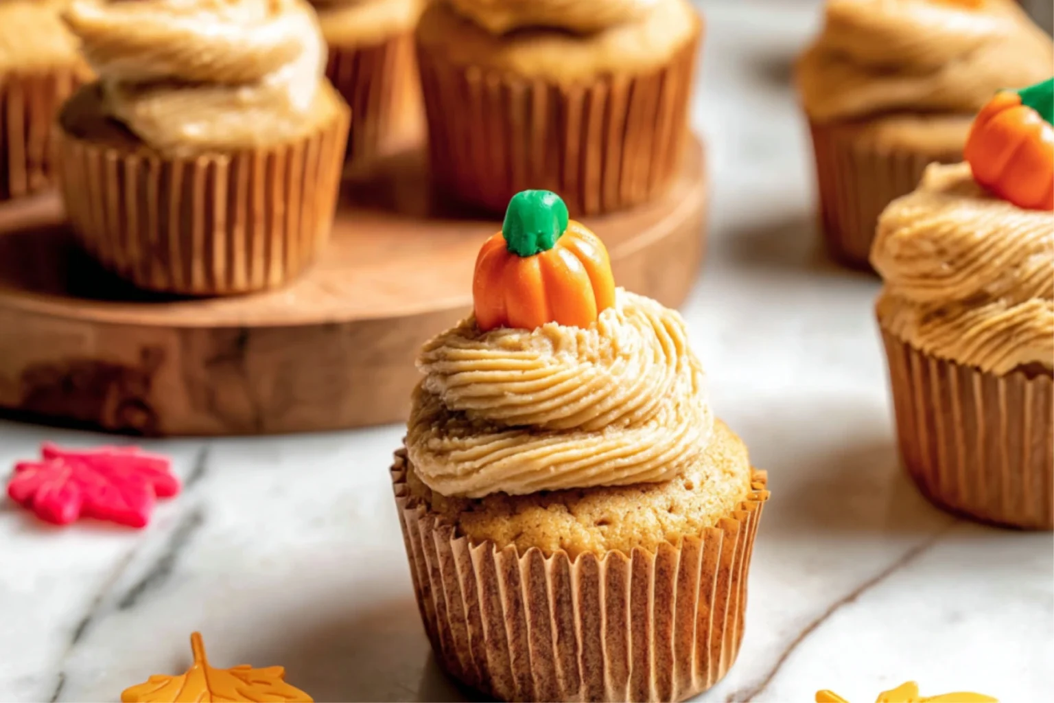 Delicious pumpkin cupcakes topped with spiced cream cheese frosting and a mini pumpkin decoration. A perfect fall dessert!