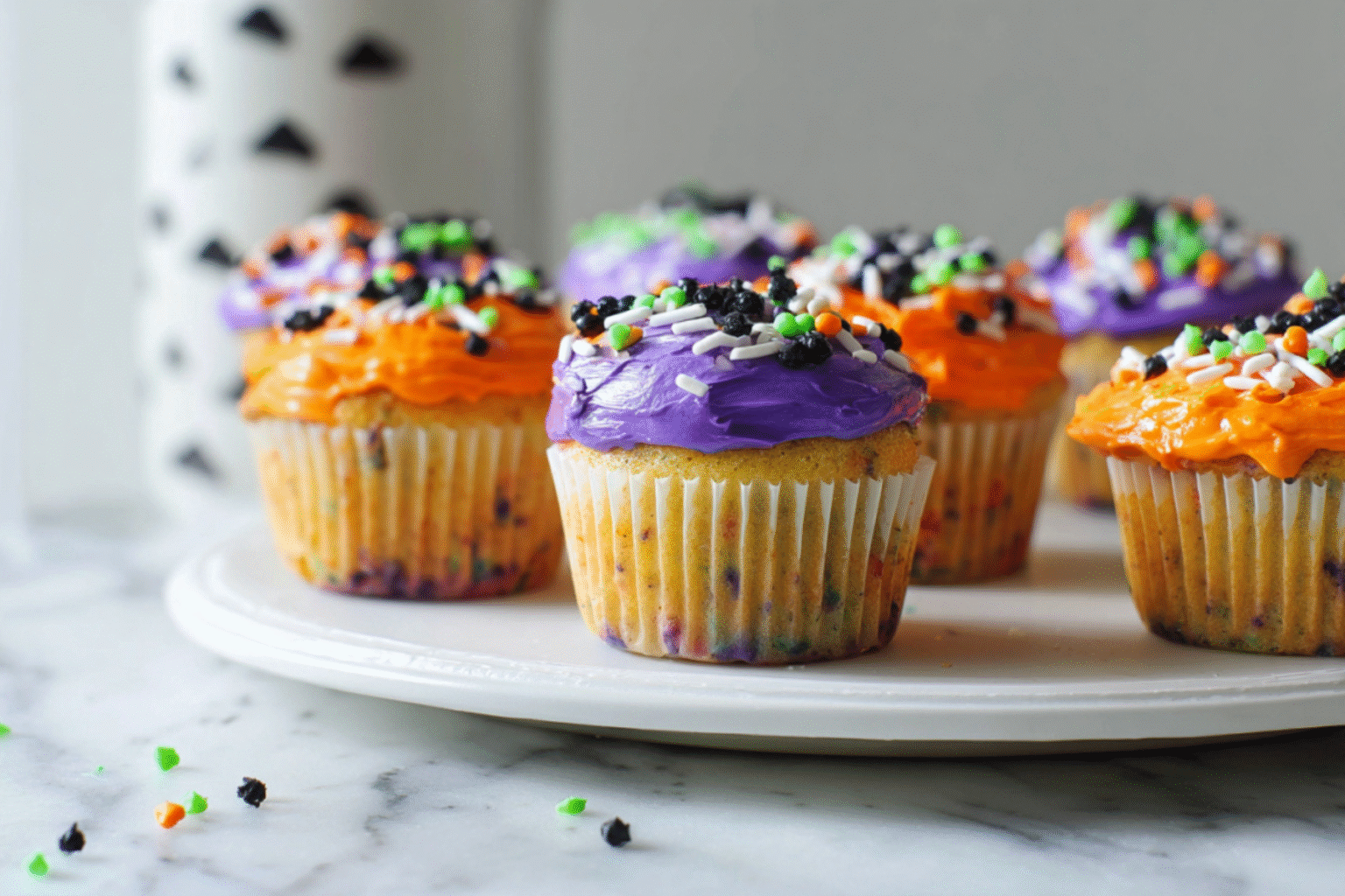 Halloween Funfetti Cupcakes with orange and purple frosting topped with Halloween sprinkles on a white plate
