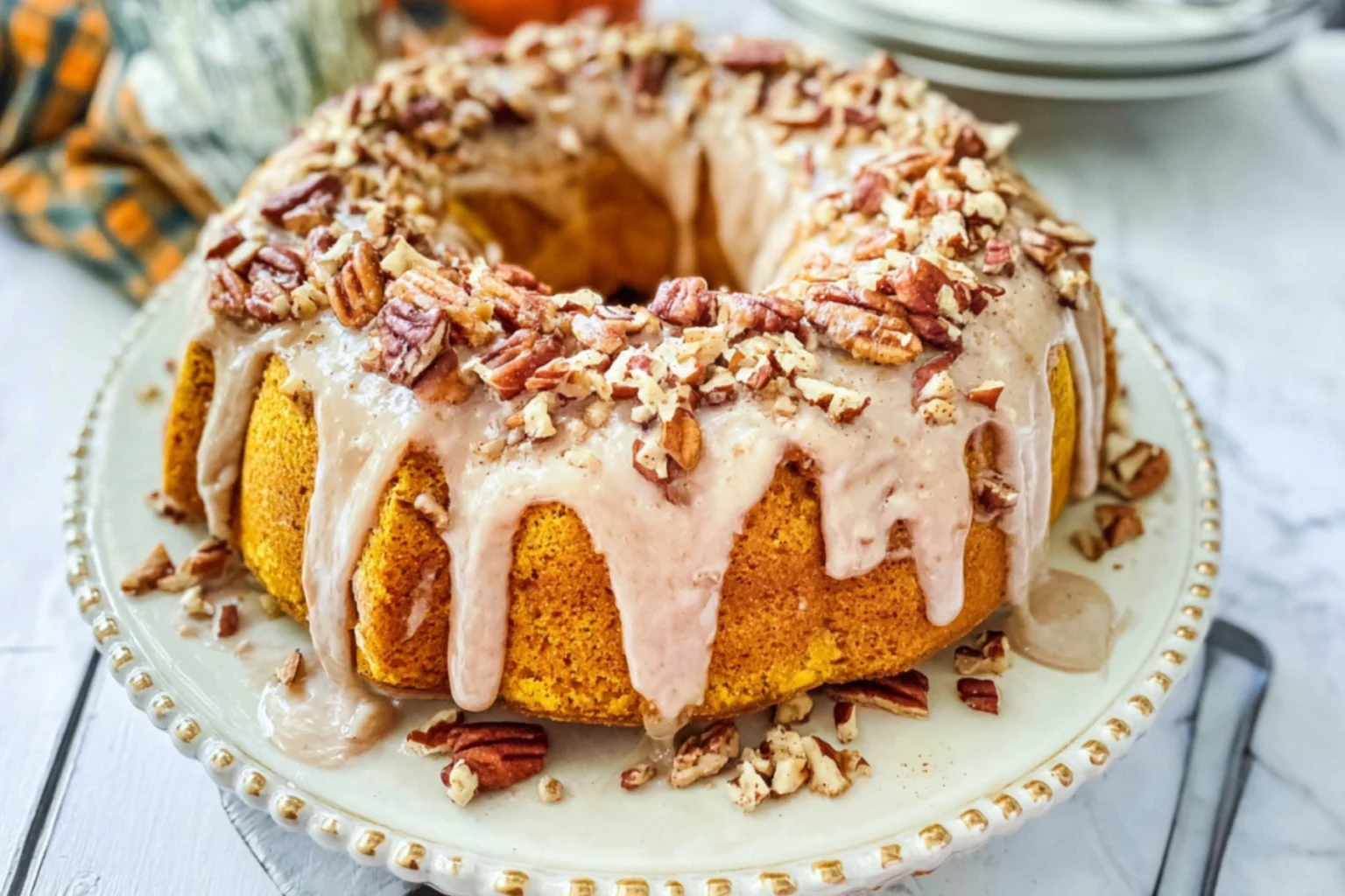 Homemade pumpkin spice bundt cake topped with creamy cinnamon glaze and chopped pecans on a decorative plate