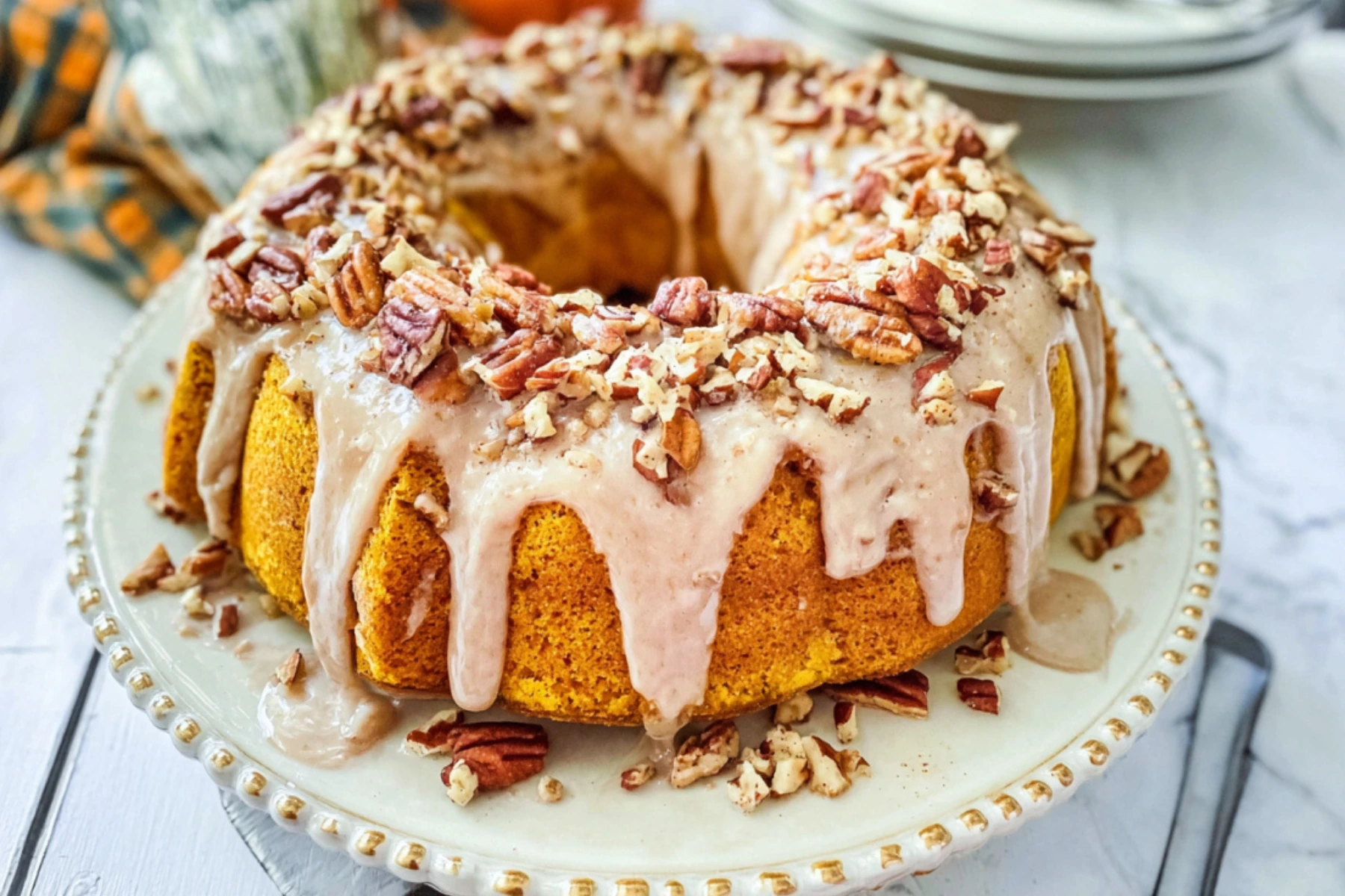 Homemade pumpkin spice bundt cake topped with creamy cinnamon glaze and chopped pecans on a decorative plate