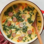 Bowl of creamy sausage, potato, and kale soup in a red Dutch oven with wooden spoon