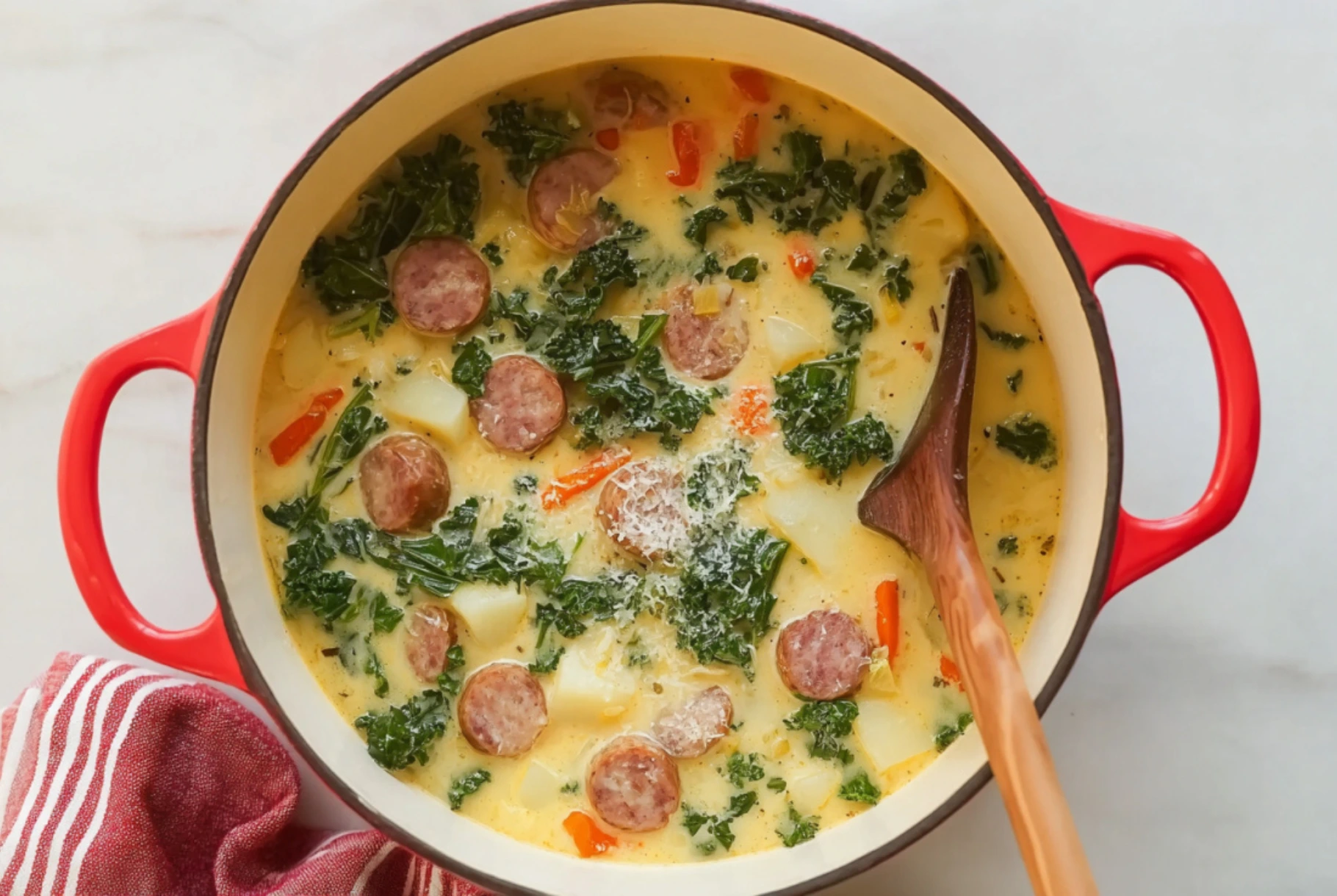 Bowl of creamy sausage, potato, and kale soup in a red Dutch oven with wooden spoon