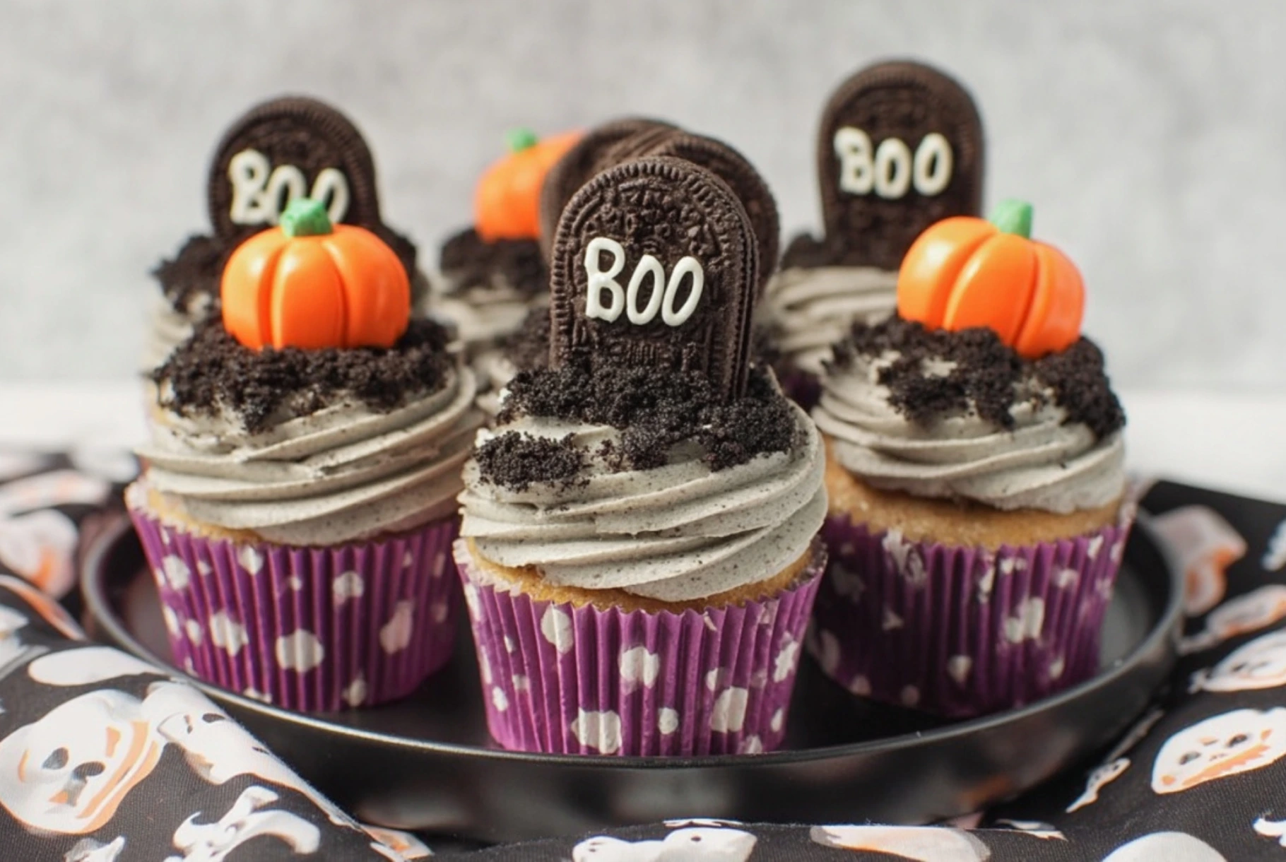 Halloween cupcakes decorated with Oreo tombstones, pumpkin toppers, and chocolate cookie crumbs.