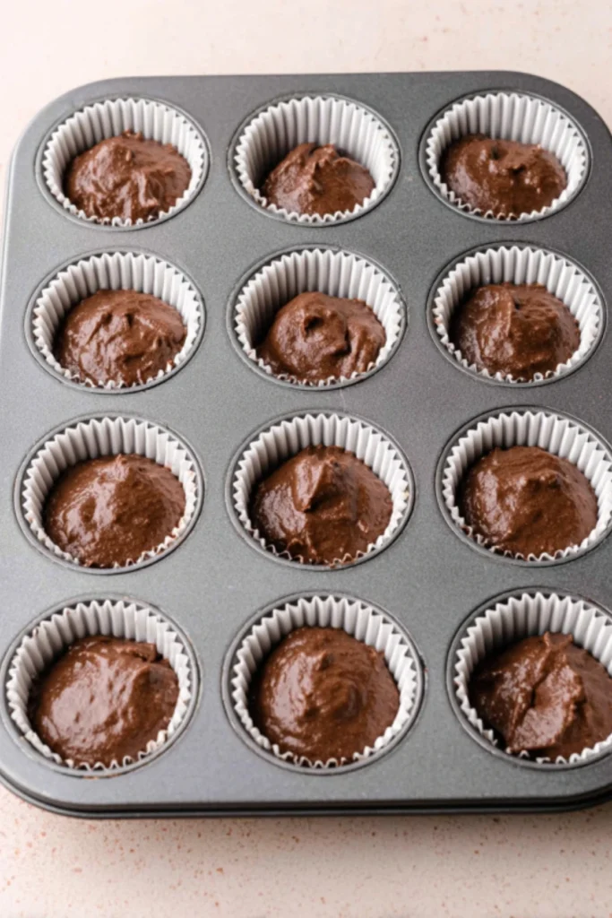 Muffin tin filled with cupcake liners and chocolate cupcake batter, ready to be baked for Candy Corn Cupcakes.