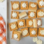 Pumpkin pie bars with creamy filling and shortbread crust topped with whipped cream and fall-shaped cookie decorations on a silver tray.