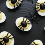 Keto Halloween Deviled Eggs topped with black olive spiders on a dark plate, perfect for a spooky low-carb Halloween snack.
