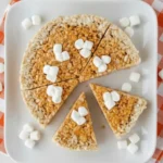 Thanksgiving Rice Krispies treats shaped like pie slices topped with mini marshmallows on a white plate with orange checkered cloth