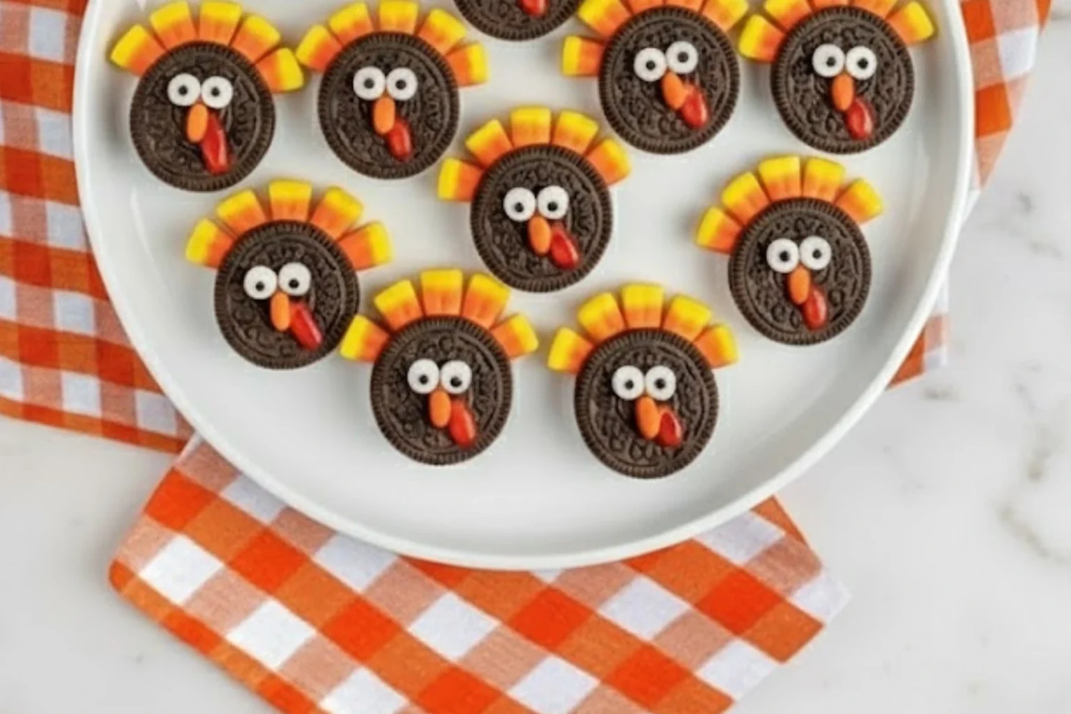 Oreo Turkey Cookies on a white plate made with candy corn, candy eyes, and Reese’s Pieces, perfect for a fun Thanksgiving dessert idea.