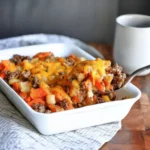 Sausage, Apple & Sweet Potato Bake with melted cheddar cheese, served on a marble countertop