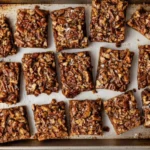 Freshly baked brown butter pecan pie bars cut into squares on a baking sheet, showing golden crust and toasted pecans.