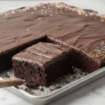 Chocolate Sheet Cake with rich chocolate frosting and colorful sprinkles on a baking pan, one slice cut and ready to serve