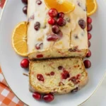 Glazed orange cranberry bread loaf topped with fresh cranberries and orange slices on a white platter