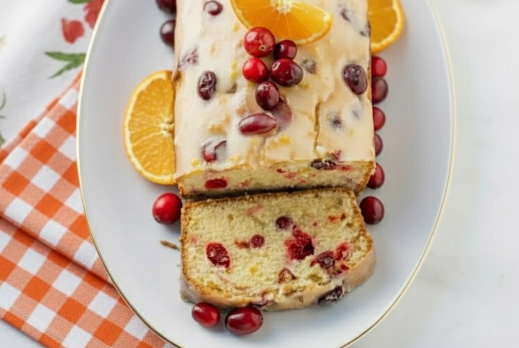 Glazed orange cranberry bread loaf topped with fresh cranberries and orange slices on a white platter