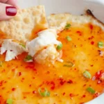 Creamy Crab Rangoon Dip topped with sweet chili sauce and green onions, served with a crispy cracker for dipping