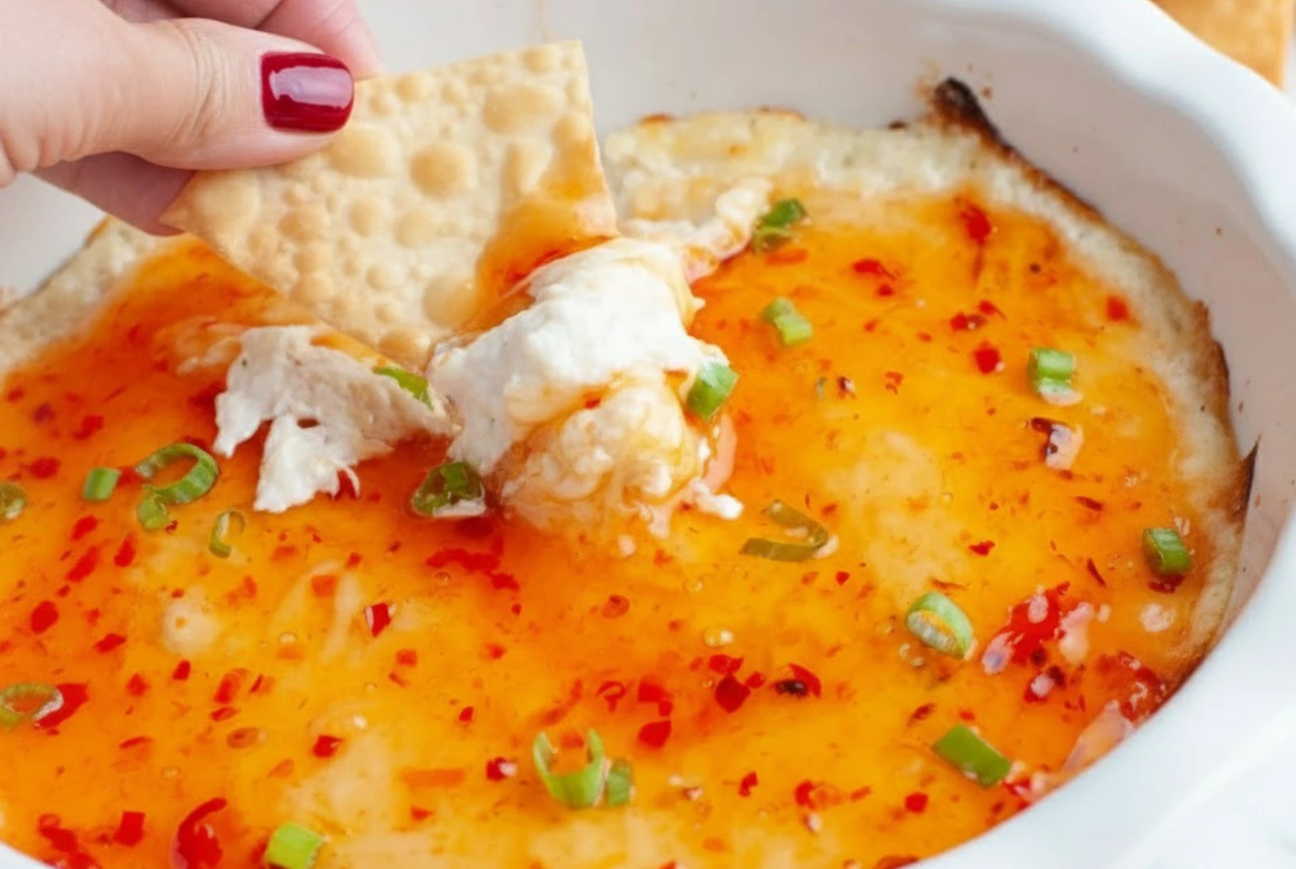 Creamy Crab Rangoon Dip topped with sweet chili sauce and green onions, served with a crispy cracker for dipping
