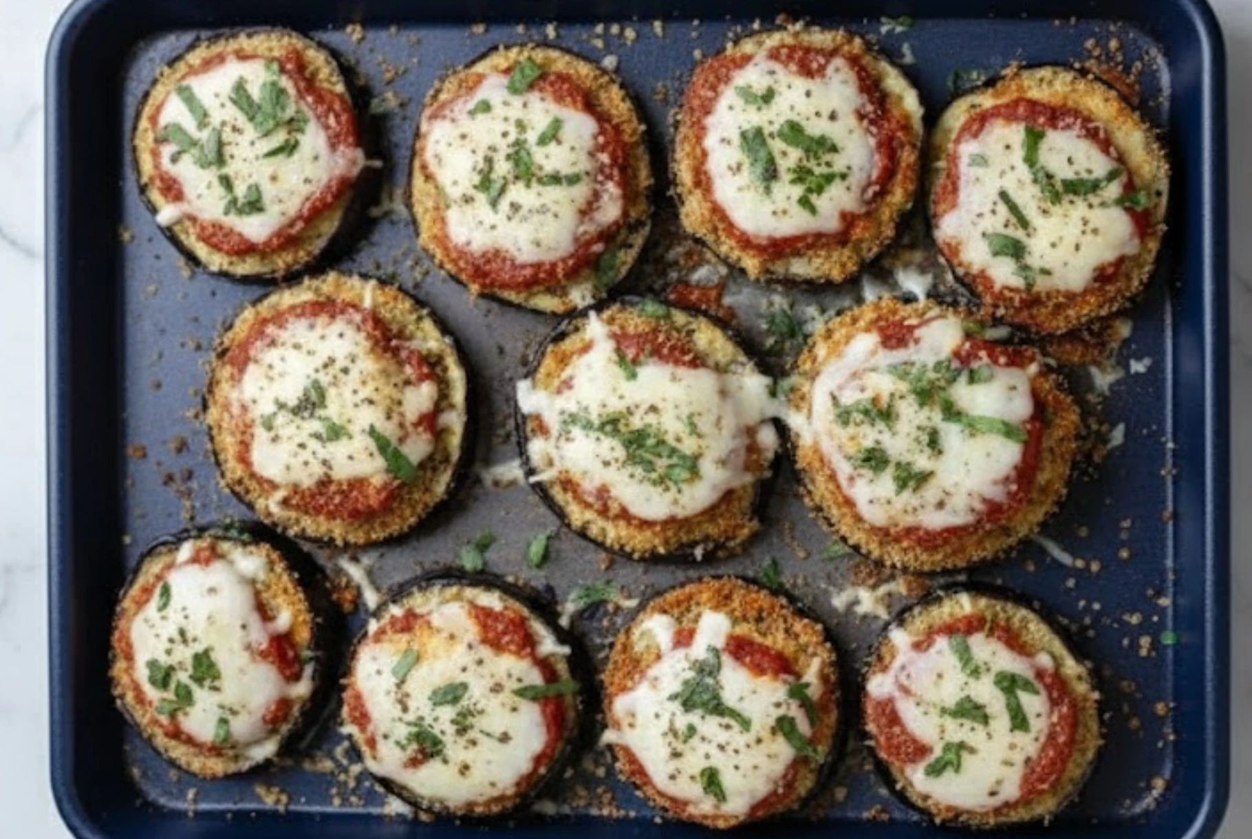 Healthy Eggplant Parmesan Bake with crispy roasted eggplant slices topped with marinara, melted mozzarella, and fresh basil on a baking tray.