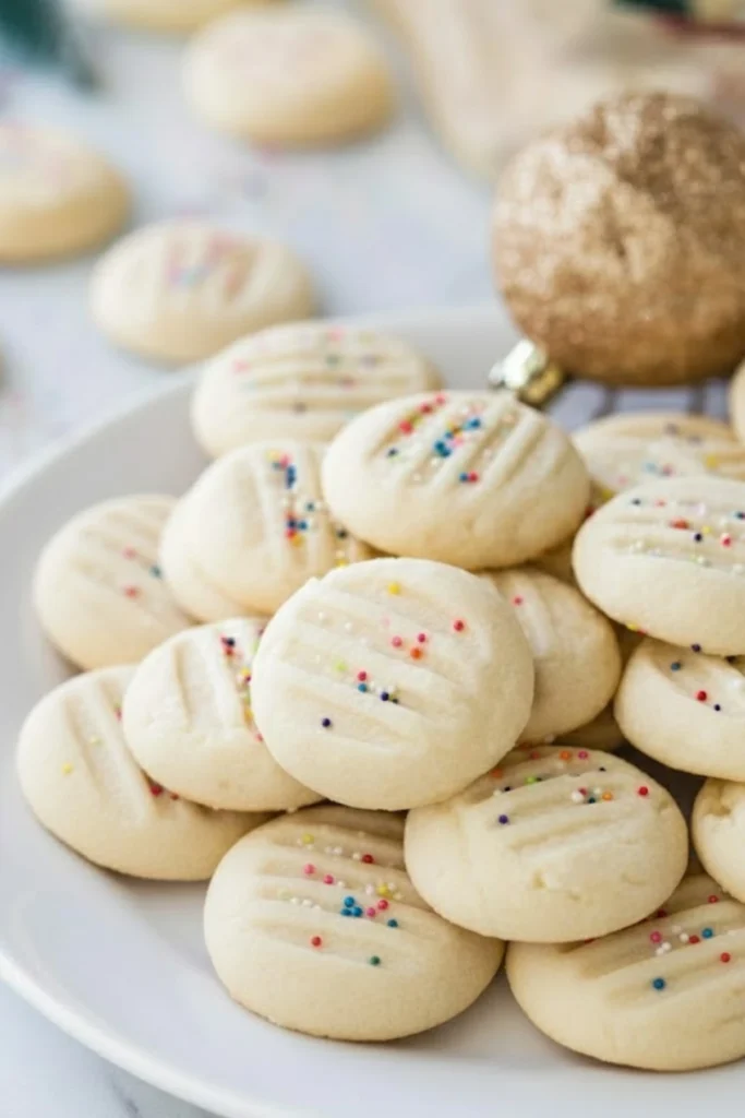 Whipped shortbread cookies topped with colorful sprinkles on a white plate, perfect for easy Christmas baking and holiday cookie trays.
