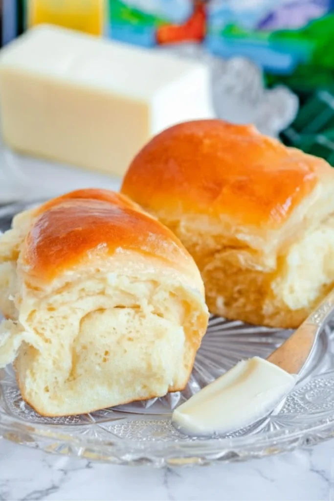 Soft Parker House Rolls on a plate with butter spread on a knife.