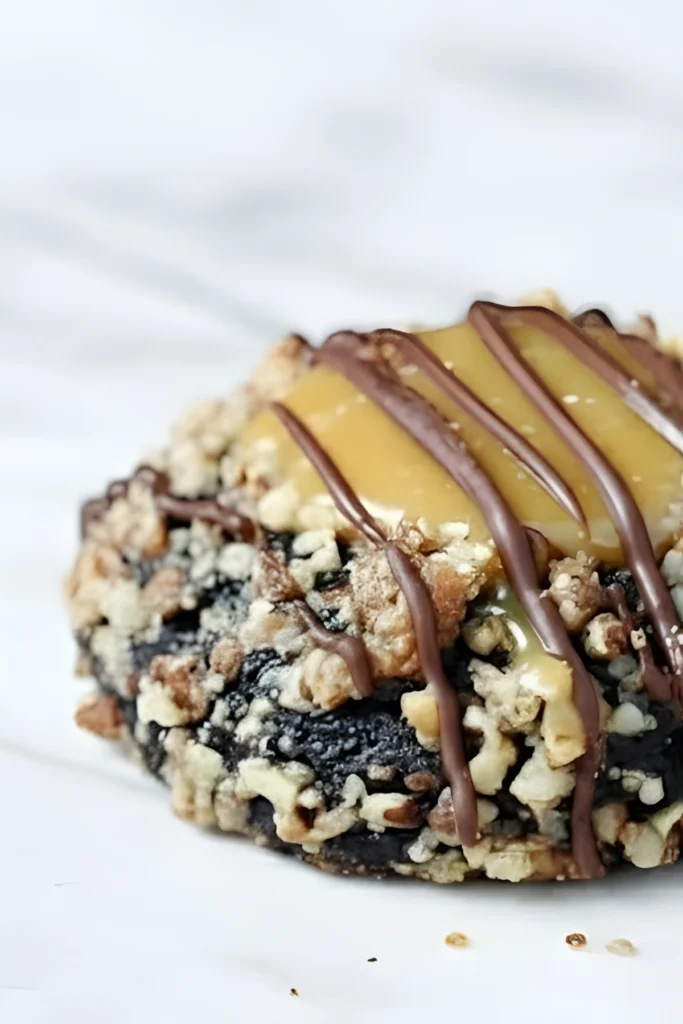 Close-up of a Turtle Thumbprint Cookie topped with gooey caramel and chocolate drizzle on a light background