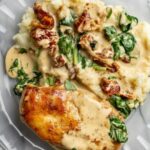 Creamy Tuscan Chicken served with spinach, sun-dried tomatoes, and mashed potatoes in a rich garlic Parmesan sauce.