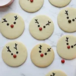 Rudolph the Red-Nosed Reindeer sugar cookies decorated with chocolate antlers and red candy noses on marble background