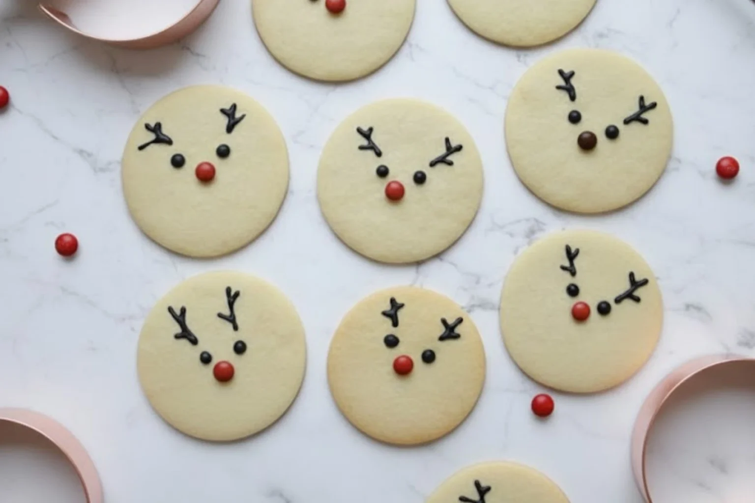 Rudolph the Red-Nosed Reindeer sugar cookies decorated with chocolate antlers and red candy noses on marble background