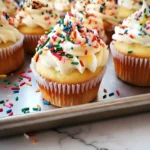 Holiday sprinkle cupcakes topped with vanilla buttercream frosting and colorful sprinkles on a baking tray, perfect for festive celebrations.