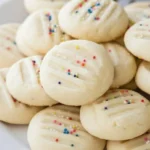 Soft and buttery whipped shortbread cookies topped with colorful sprinkles, freshly baked and served on a white plate for the holidays.