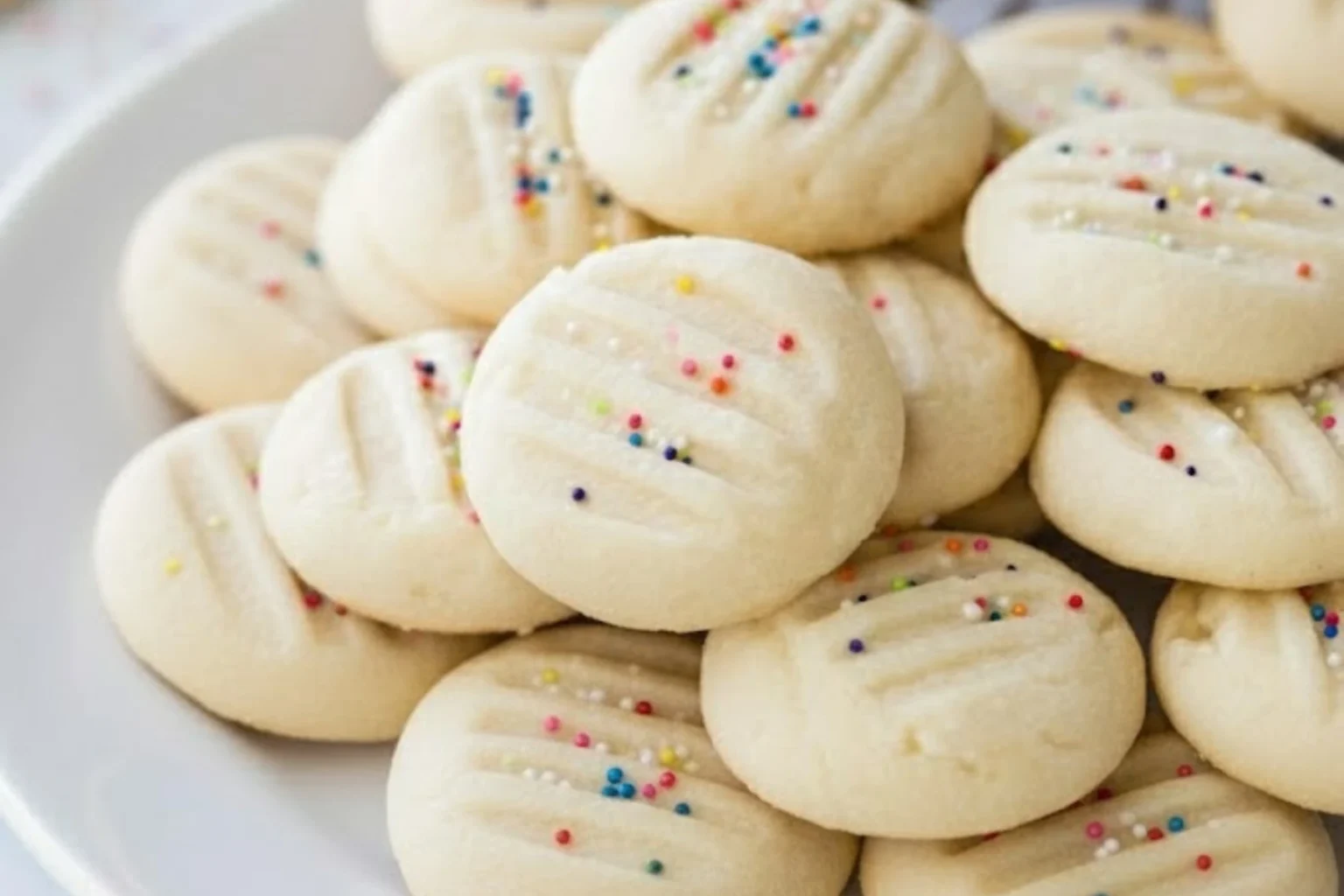 Soft and buttery whipped shortbread cookies topped with colorful sprinkles, freshly baked and served on a white plate for the holidays.