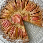 Caramel Apple Tart with thinly sliced apples arranged in a spiral pattern on a golden crust, dusted with powdered sugar on a glass plate.
