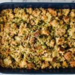 Golden baked herb stuffing for Thanksgiving in a blue casserole dish with crisp bread cubes, fresh herbs, and buttery texture.