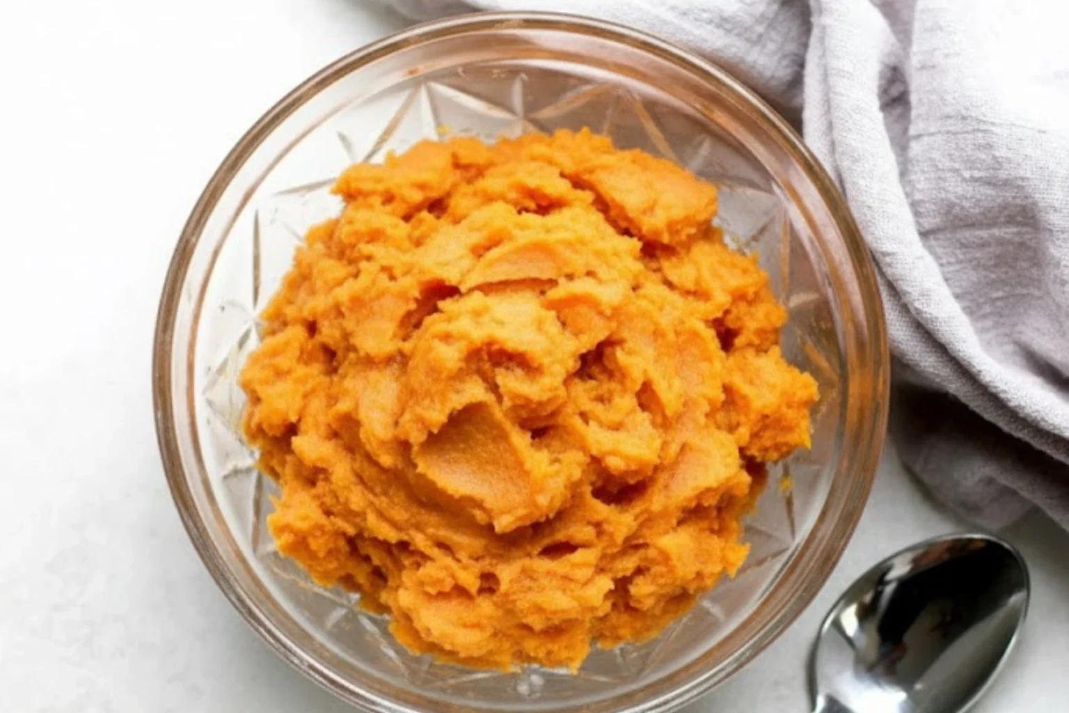 Bowl of brown butter whipped sweet potatoes on a light surface with a spoon nearby.